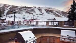 An outdoor kitchen with a grill and a water feature, surrounded by stone walls and a view of a snowy mountain and ski lift. - Marriott's MountainSide (Studio) (Park City)