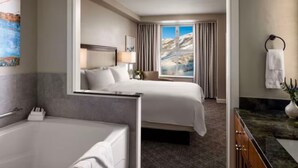 A hotel room with a large bed, a bathroom with a bathtub, and a view of mountains through the window. - Marriott's MountainSide (1BR) (Park City)