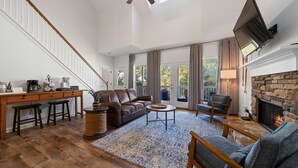 Un salón amplio con chimenea, ventilador de techo y un ventanal grande.