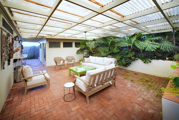 Un patio couvert aménagé avec un canapé en bois, des fauteuils et une table basse.
