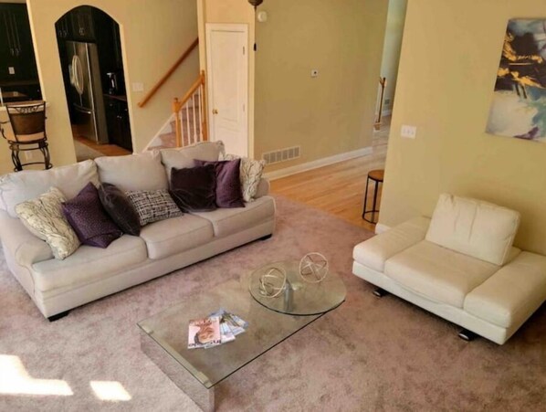 A living room with two sofas, a glass coffee table, and a staircase in the background.