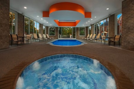 An indoor swimming pool area with lounge chairs and a hot tub.