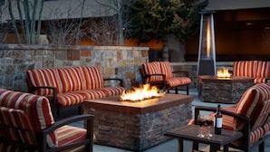 Un patio al aire libre con muros de piedra, sofás a rayas y una chimenea central.