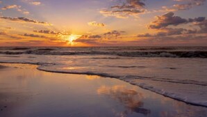 Ein Strand bei Sonnenuntergang, wobei Wellen den Himmel spiegeln.