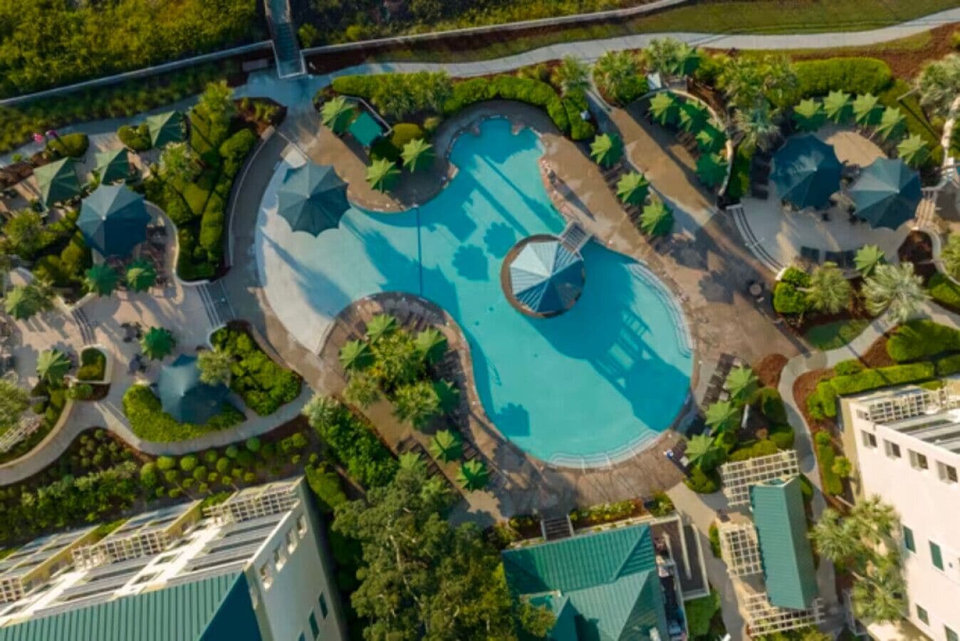 An aerial view of a resort with multiple swimming pools, surrounded by lush greenery and pathways.