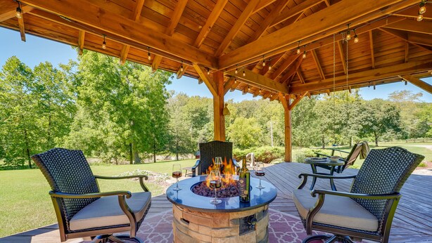 A covered outdoor seating area with a stone fire pit, two chairs, and a table. - Game Room & Deck: Serene Ava Countryside Home (Ava)