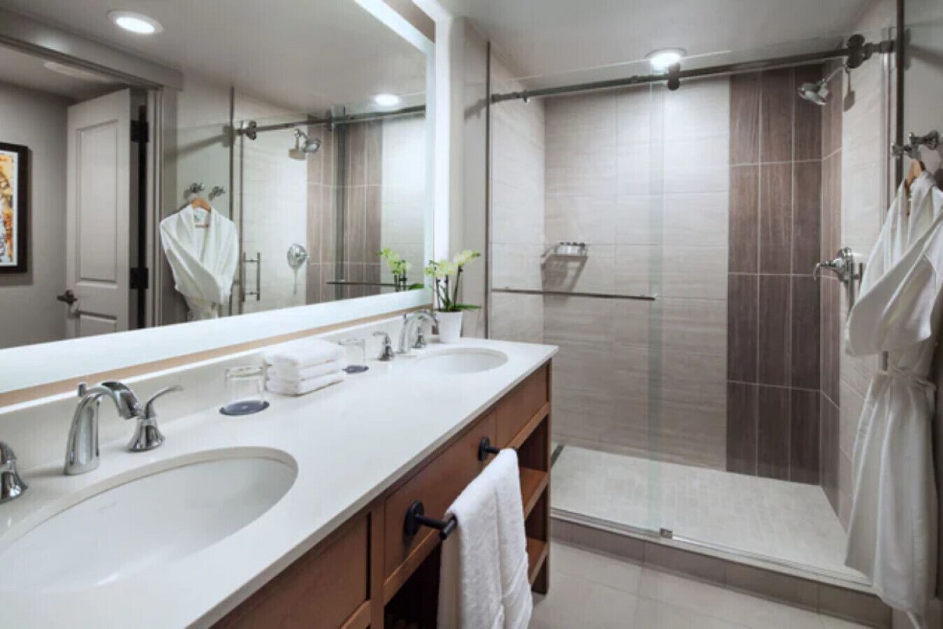 A modern bathroom with two sinks, a large mirror, and a glass-enclosed shower area.