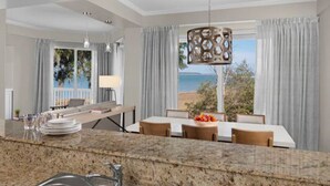 A modern kitchen with granite countertops, a dining area with a table and chairs, and a view of the sea through large windows.
