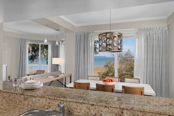 A modern kitchen with granite countertops, a dining area with a table and chairs, and a view of the sea through large windows.