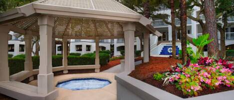 A gazebo with a hot tub, surrounded by a garden with various plants and flowers.