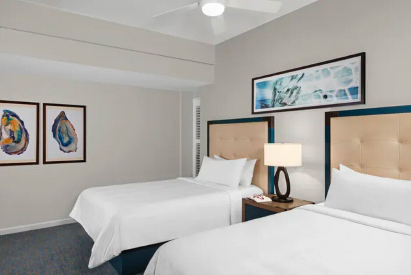 A hotel room with two beds, a ceiling fan, and artwork on the walls.