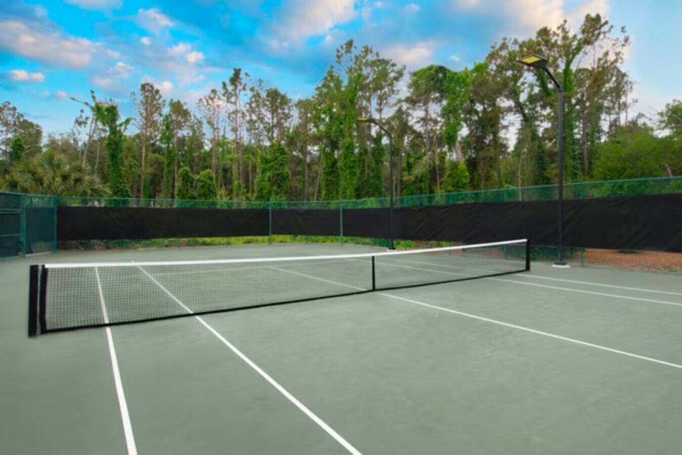 A tennis court with a net, surrounded by trees and a fence.