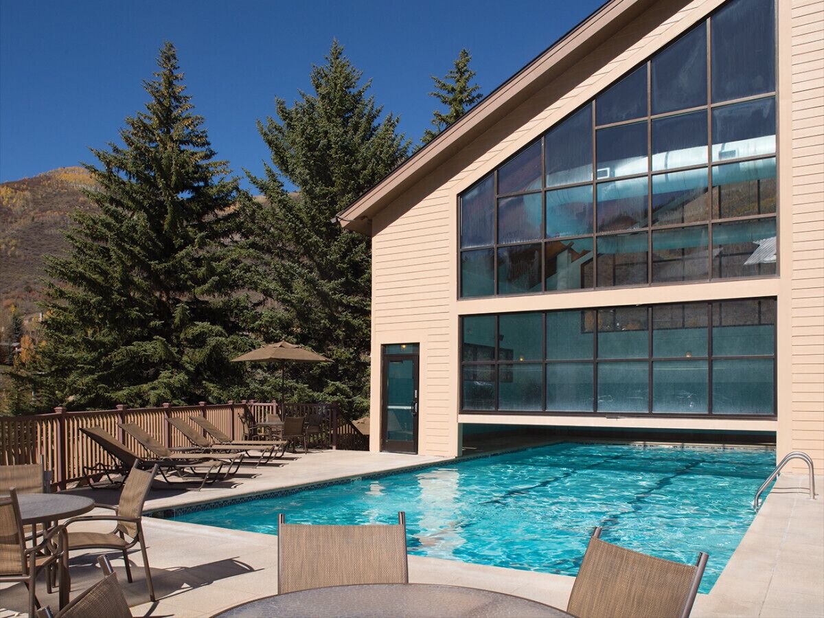 A modern building with a large glass window, a swimming pool, and outdoor seating.