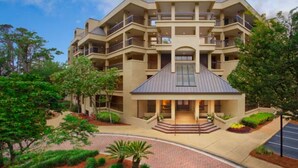 A multi-story hotel with a central atrium, balconies on each floor, and a landscaped entrance area.