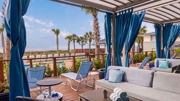 A covered outdoor seating area with a pool, lounge chairs, and a sofa. - Marriott's SurfWatch (2BR) (Hilton Head Island)
