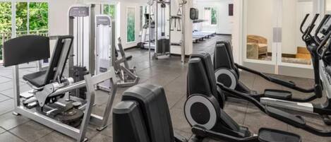 Un gimnasio con varios equipos de ejercicio, incluyendo cintas de correr, elípticas y máquinas de pesas.