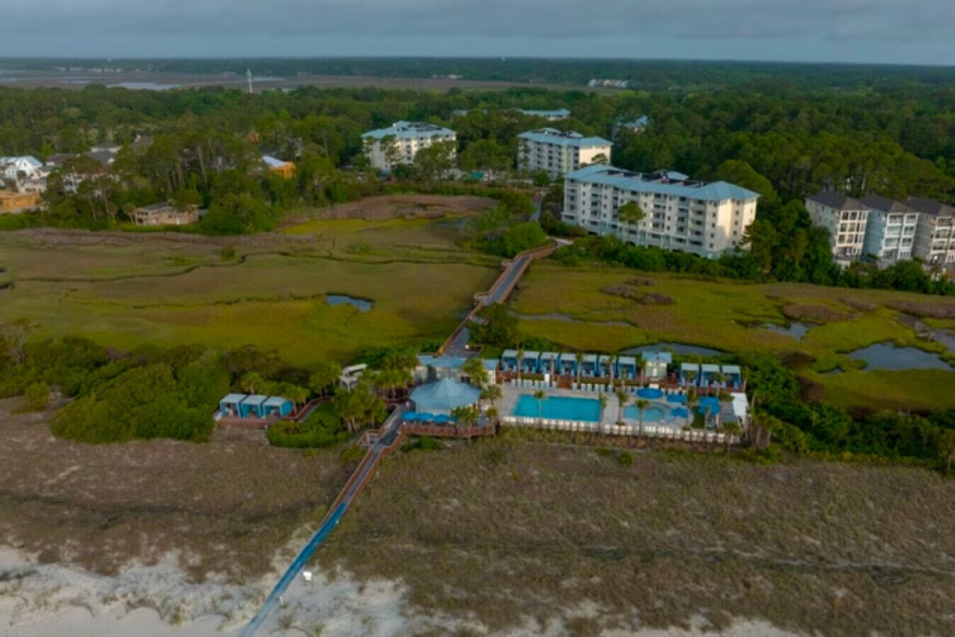Vista aerea di un resort con diversi edifici, un'area piscine centrale e paesaggi naturali circostanti.