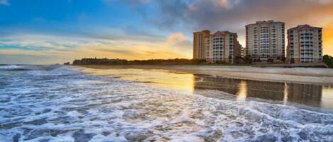 A beach with waves and a row of high-rise buildings in the background.