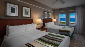 A hotel room with two beds, a ceiling fan, framed artwork on the wall, and a view of the ocean. - OceanWatch (2 Bedroom) (Myrtle Beach)