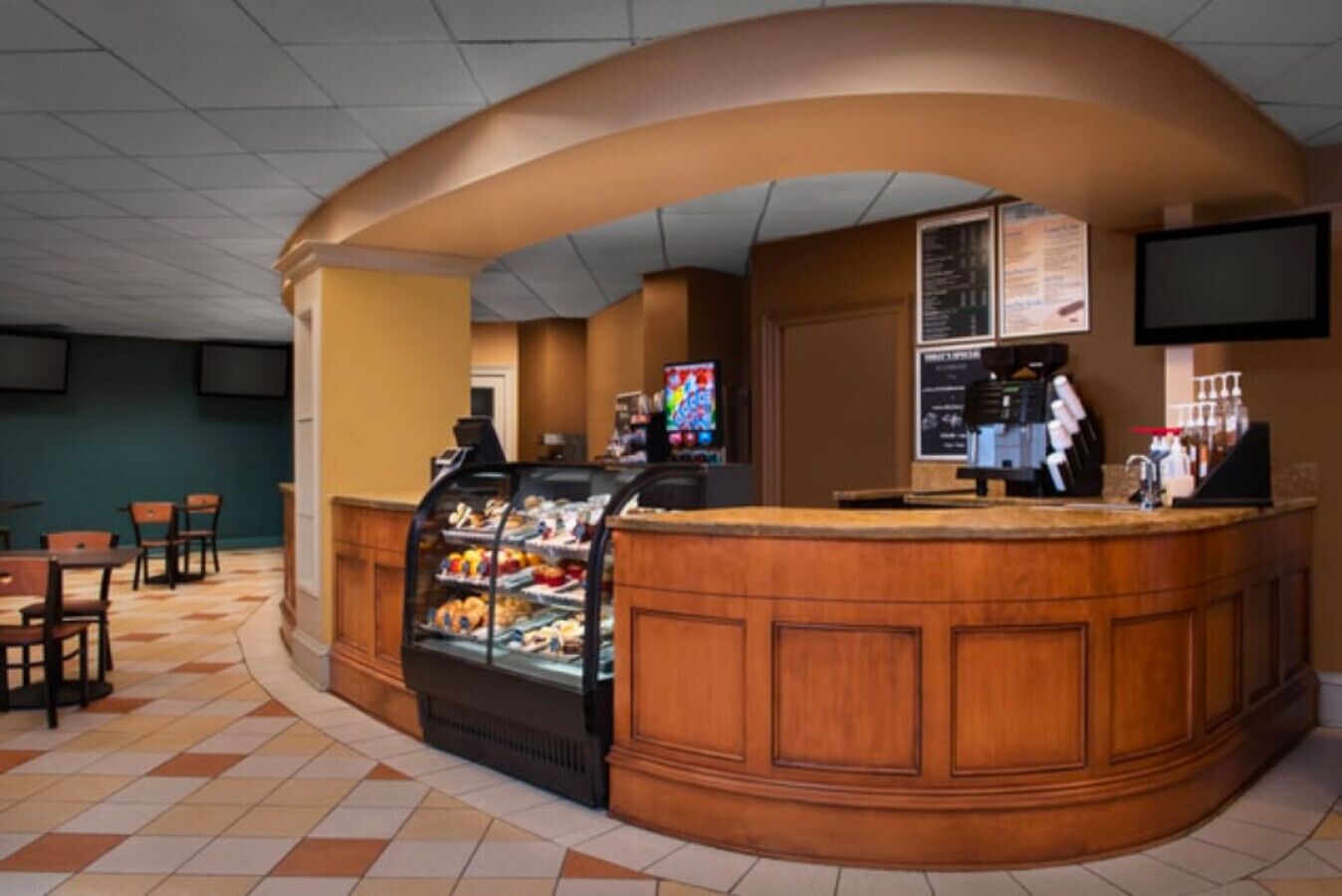 Un comptoir de boulangerie avec une vitrine remplie de pâtisseries, une machine à café et un tableau affichant le menu.