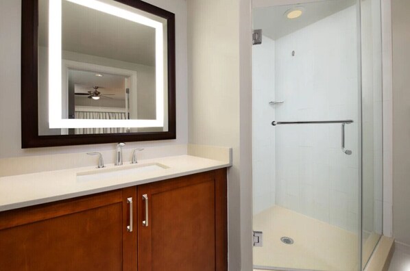 Un baño con lavamanos blanco, mueble de madera y ducha con mampara de vidrio.