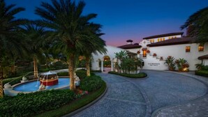 Un hotel con una fuente, palmeras y un patio empedrado.