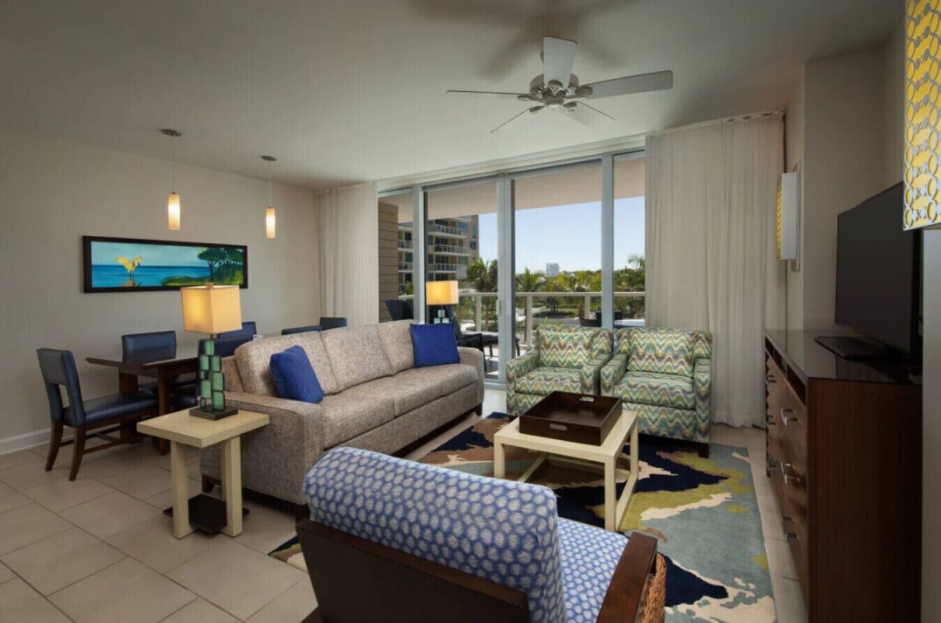 A hotel room with a sofa, armchair, TV, and a balcony with a view.