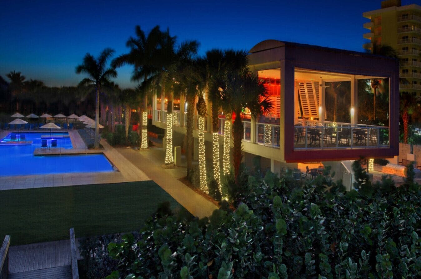 A modern hotel with a pool, palm trees, and string lights.