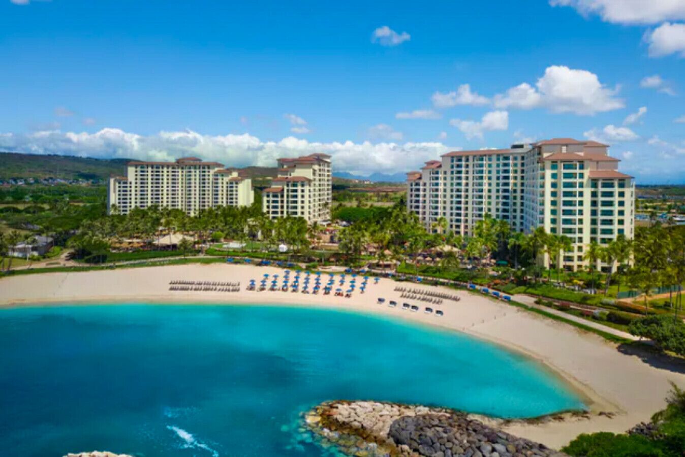 A resort with multiple high-rise buildings, a sandy beach with umbrellas, and a clear blue ocean.