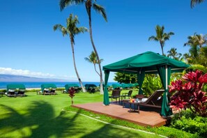 Relax on the beachfront lawn with a gazebo, lounge chairs, and lush greenery.