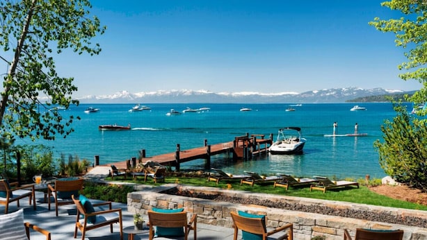 A waterfront patio with wooden chairs and tables, a dock with boats, and a clear view of the sea and mountains in the background. - The Ritz-Carlton Club, Lake Tahoe (3 Bedroom) (Truckee)
