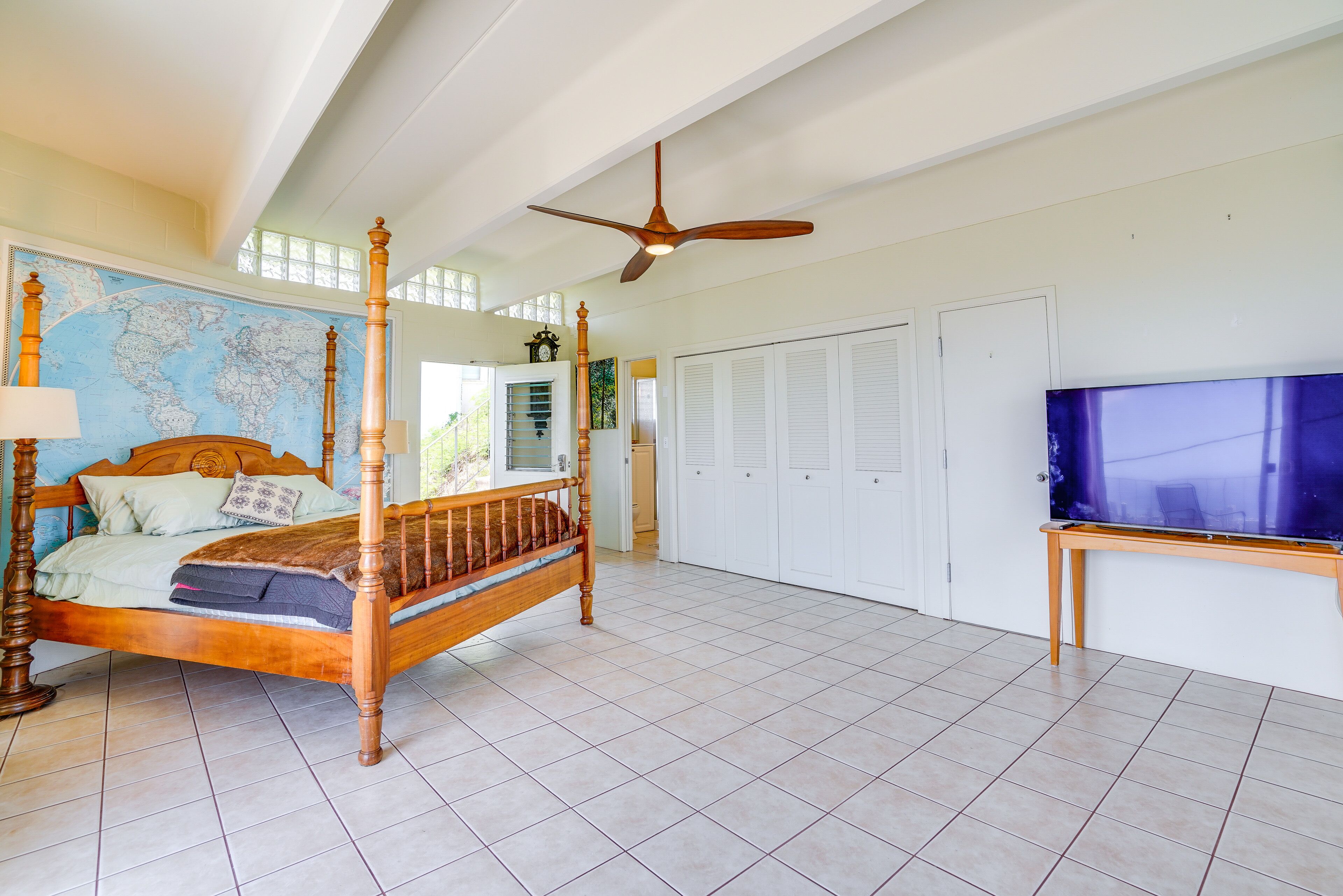 A spacious bedroom with a large bed, a ceiling fan, a map on the wall, and a TV on a stand.