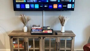 Un mobile contenitore in legno con ante in vetro, una TV a schermo piatto montata sopra che mostra diversi servizi di streaming, e due vasi con piante essiccate su entrambi i lati.