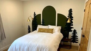 Un letto rifatto con cura, lenzuola bianche e un solo cuscino decorativo, un comodino e una parete con un murale a tema naturalistico.
