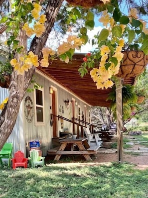 A rustic cabin with a wooden porch, a dining table, and outdoor seating.