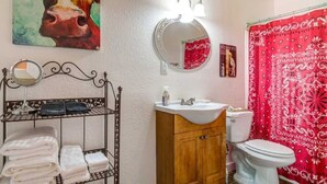 A bathroom with a round mirror, a sink, a toilet, and a towel rack with folded towels. - #2 Forge~Bandera Tin Star~Bandera, TX~Country (Bandera)