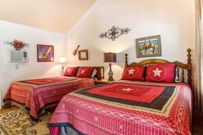 A bedroom with two beds, each with red bedding and star patterns, a wooden headboard, and a wall-mounted lamp. - #2 Forge~Bandera Tin Star~Bandera, TX~Country (Bandera)