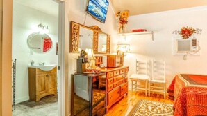 A bedroom with a bed, a dresser, a mirror, a television, and a small window with an air conditioner. - #2 Forge~Bandera Tin Star~Bandera, TX~Country (Bandera)