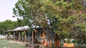 A rustic cabin with a porch, picnic tables, and a large tree. - #2 Forge~Bandera Tin Star~Bandera, TX~Country (Bandera)