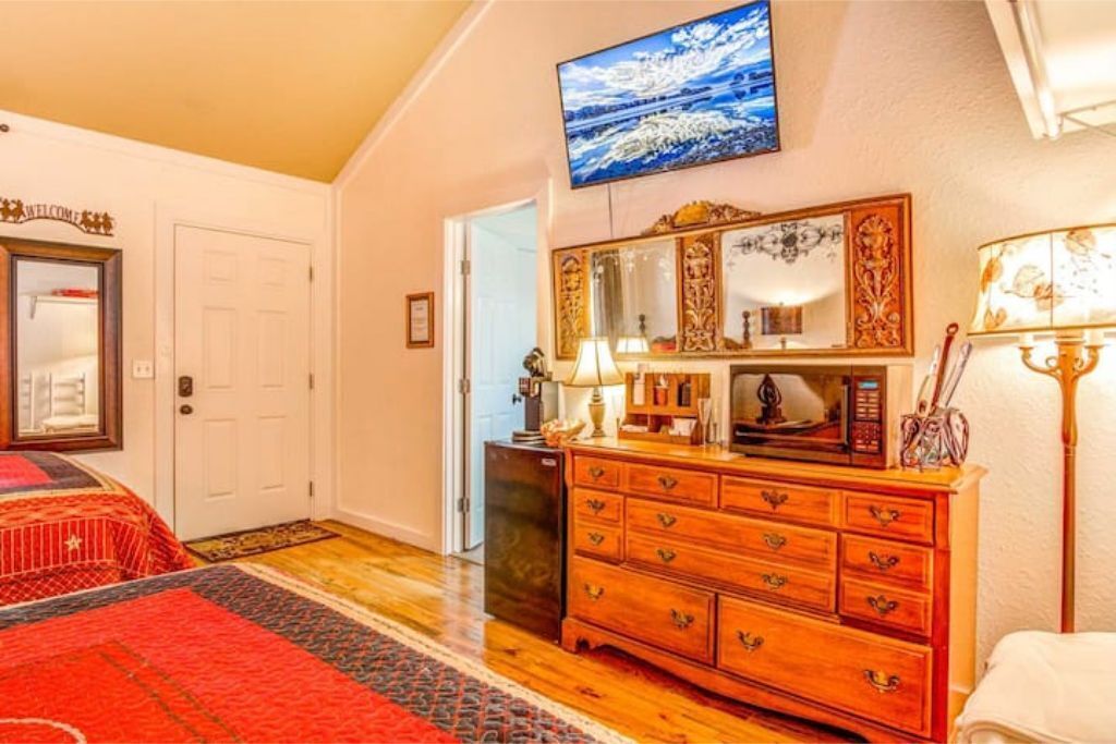 A hotel room with a wooden dresser, a television mounted on the wall, and a red and black patterned rug.