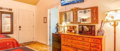 A hotel room with a wooden dresser, a television mounted on the wall, and a red and black patterned rug.