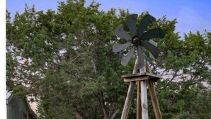 A rustic wooden windmill structure in a rural setting with a barn and trees in the background. - #2 Forge~Bandera Tin Star~Bandera, TX~Country (Bandera)