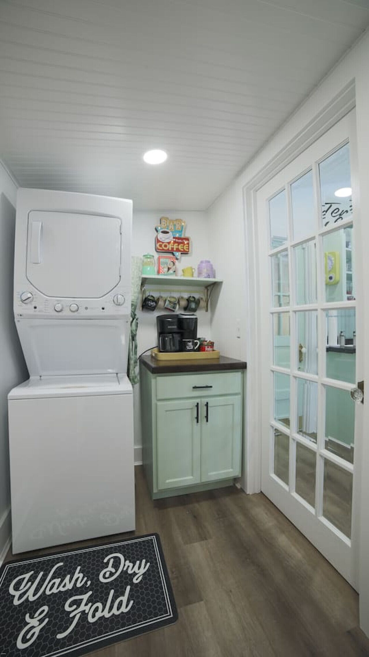 A compact kitchen with a washing machine, a coffee station, and a cabinet.