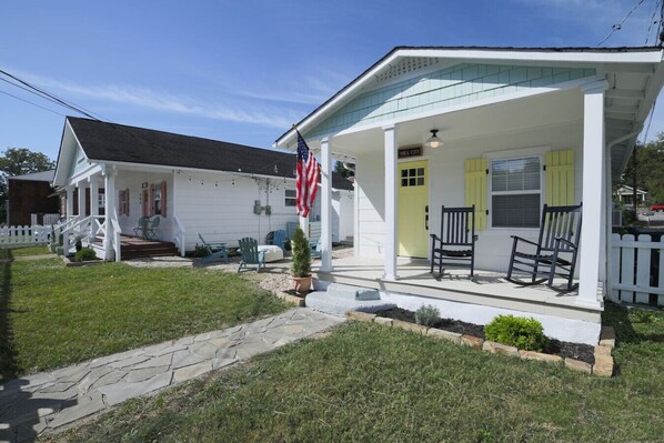 A white house with a porch, a small garden, and an American flag.