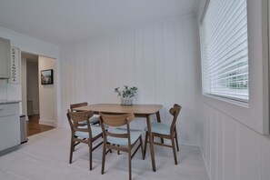 Ein Essbereich mit einem Holztisch und vier Stühlen, einer Topfpflanze auf dem Tisch und einem Fenster mit Jalousien.