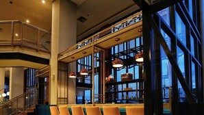 A bar area with hexagonal patterned flooring, a staircase, and a view through large windows. - Patra Malioboro (Gedong Tengen)