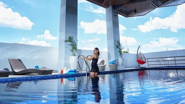 A swimming pool with lounge chairs and a person standing by the pool. - Patra Malioboro (Gedong Tengen)