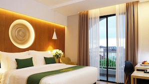 A hotel room with a large bed, a desk, a chair, a window with curtains, and a view of the city. - Patra Malioboro (Gedong Tengen)