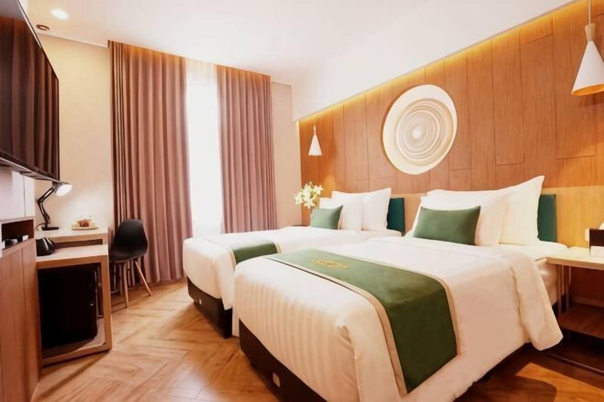 A hotel room with two beds, a desk, a chair, and a TV.