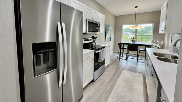 A modern kitchen with stainless steel appliances, white cabinetry, and a dining area with a view of the outdoors. - New Construction Townhome - 3 King Beds/2.5 Bathroom! (Cedar Falls)